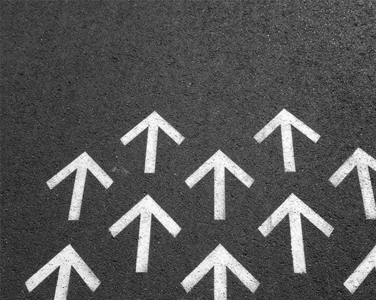 An image of white arrows pointing upwards on a black asphalt road.