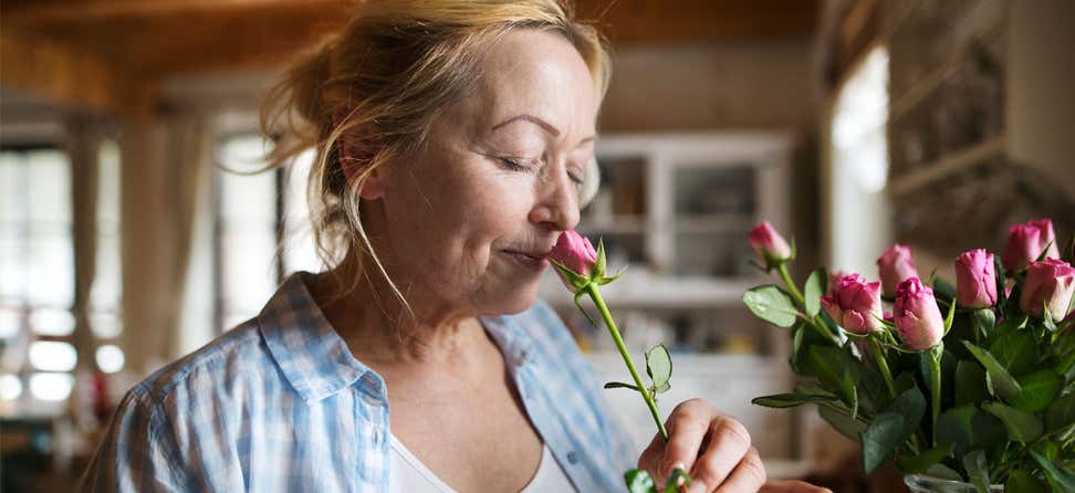 An older Caucasian woman is taking time to sleep the roses in her kitchen.
