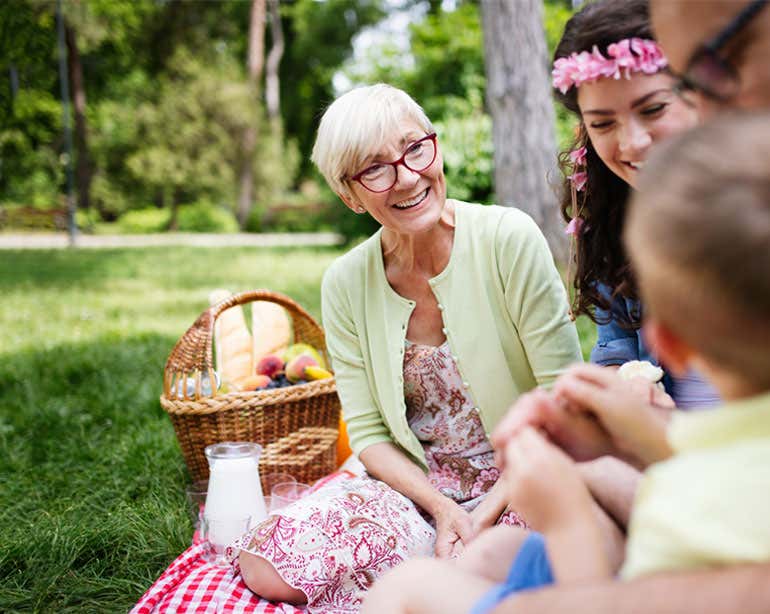 A senior woman sits with her family at a picnic in the park.