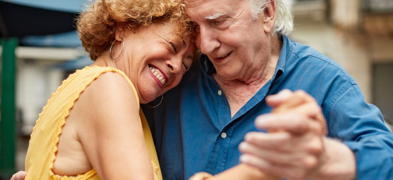 An upclose shot of a senior couple dancing outside, close together.