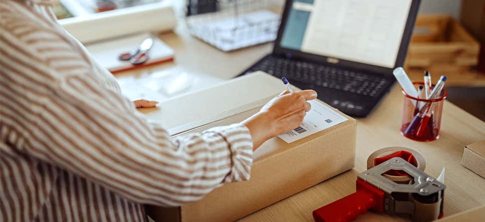 A senior center female professional is labeling a package for outgoing mail.