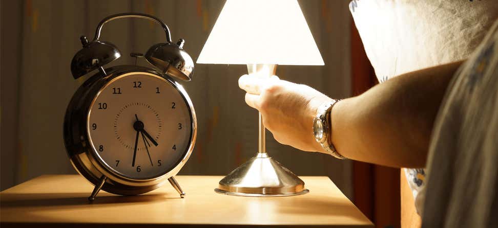 A senior woman in bed is turning off her lamp, indicating that she's going to sleep.