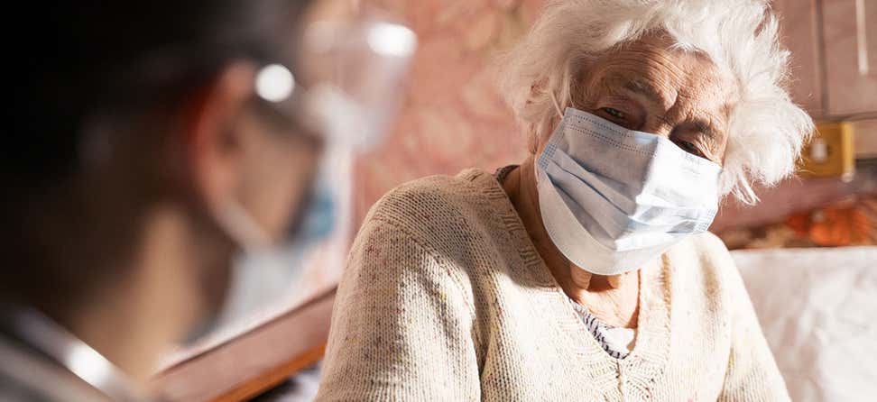 senior masked woman talking with her healthcare provider at home