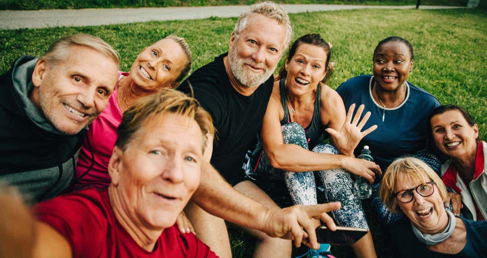 A group of multi-generational adults pose for a selfie while outside at the park.