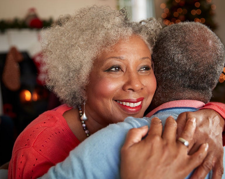 A close up shot of a Black senior woman smiling as she hugs her companion.