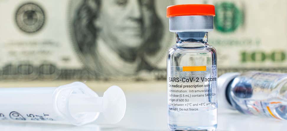 A SARS COVID-19 vaccine vial and syringe appear in a close up in front of a one-hundred U.S. dollar bill.