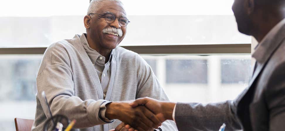 A senior Black man is shaking hands with a professional offering a debt management plan. A debt management plan can provide relief by rolling several of your credit card balances into a single, manageable monthly payment.