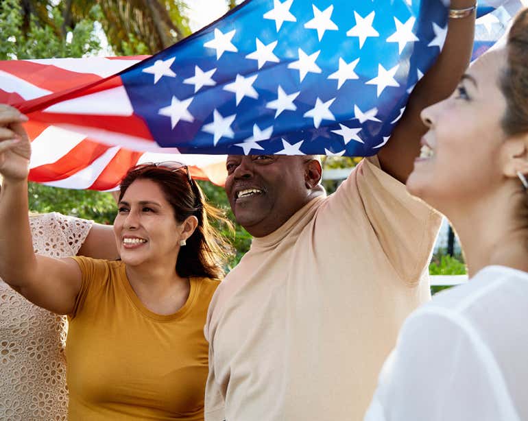 A multi-ethnic group of friends are holding an American flag and enjoying a holiday celebration.
