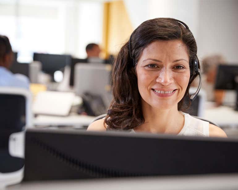 An older female professional is sitting at her desk with her headset on, taking phone calls from Medicare beneficiaries.