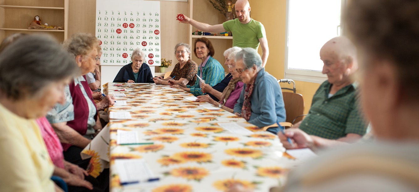 A group of older adult women are playing Bingo in a senior center during the day.