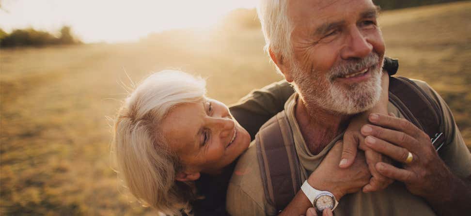A senior caucasian couple is embracing each other outside as they walk together during sunset.