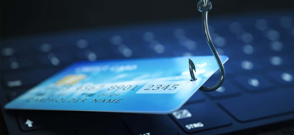A fishing hook is stuck into a credit card over a computer, indicating phishing.