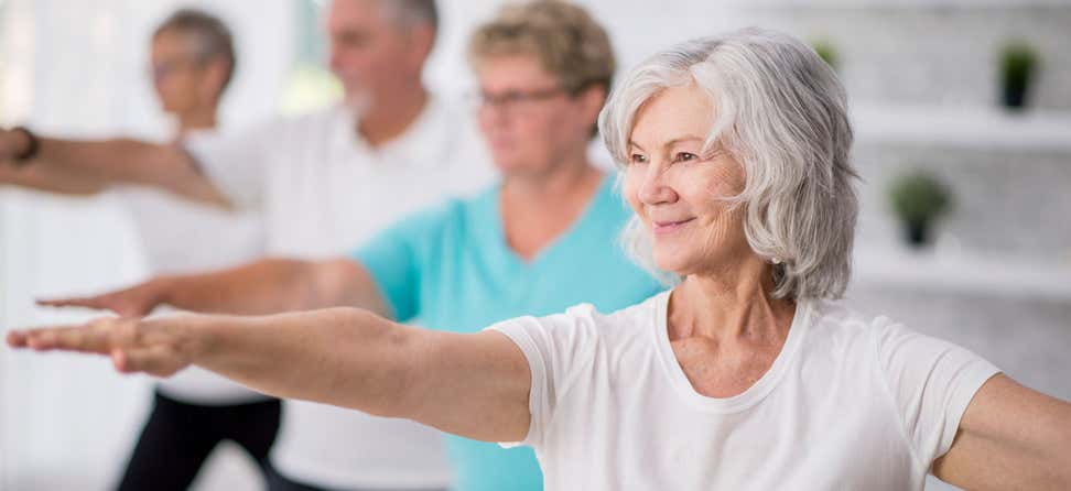 An older woman smiling is doing yoga in a group setting.