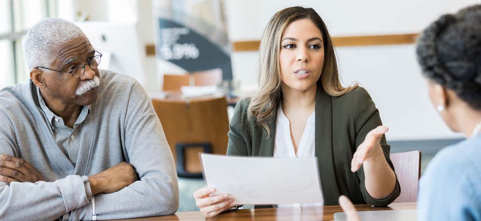 A mid-adult female advocate gestures while meeting with a policymaker about issues that affect her older father's future.