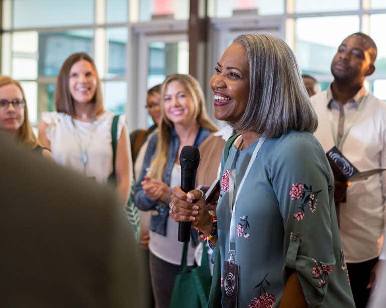 An older African American woman holds a mic in her hand while she's asking a question at a town hall.