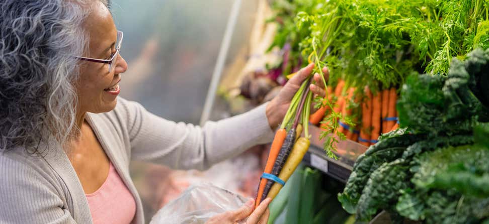 A senior Black woman is picking out carrots in the produce section.