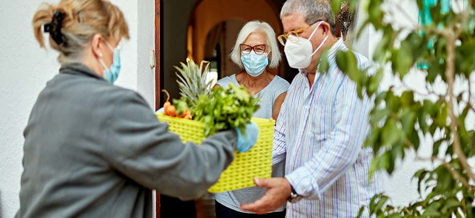 senior masked caucasian couple receives a grocery delivery at home during the COVID-19 quarantine