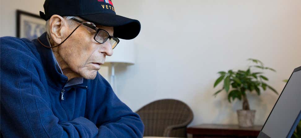 A retired Veteran is looking intensely at his laptop computer at his kitchen table.