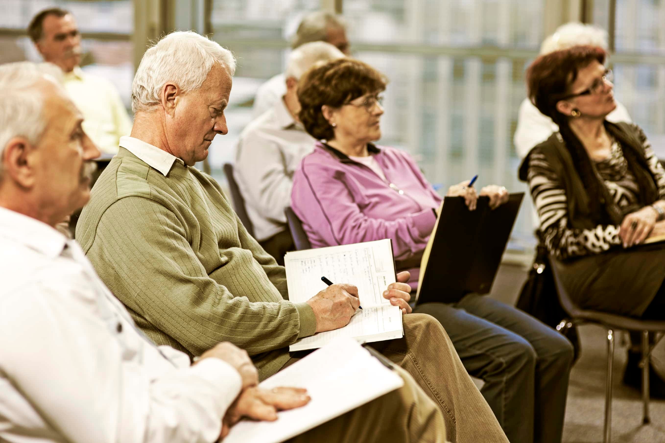 A group of seniors is in a classroom setting, taking notes while a speaker is presenting.