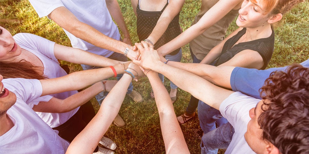 A group of multi-generational people have their hands in a huddle, signifying teamwork.
