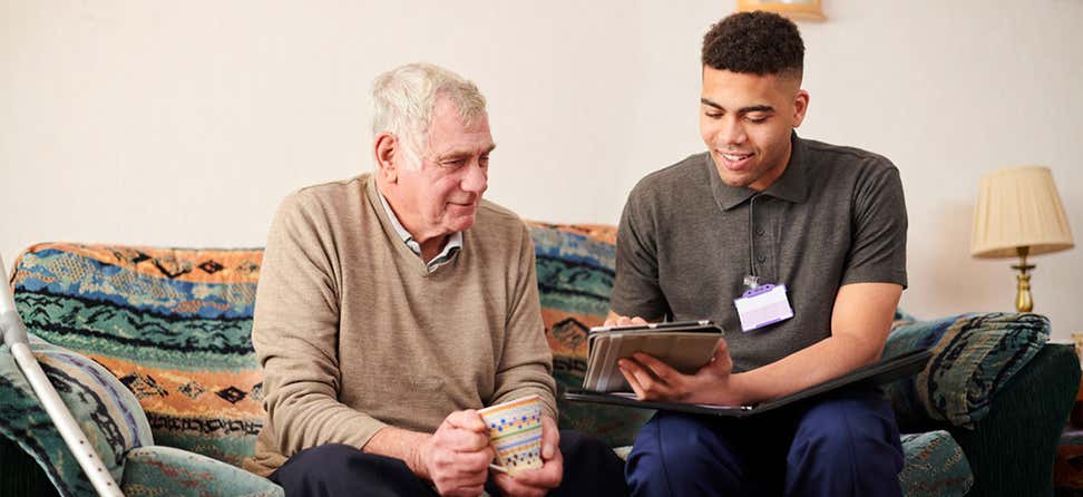 A younger aging services professional is in the home of a senior man, going over his options for at-home care.