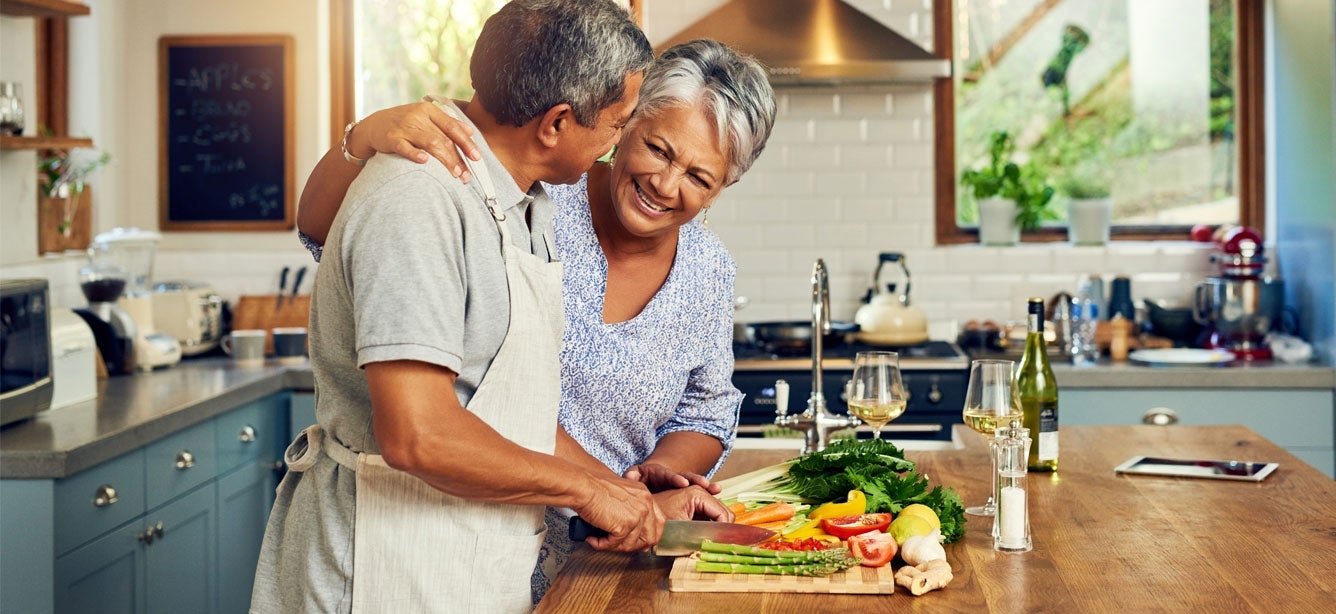 A Black senior couple is preparing a meal together in their home kitchen.