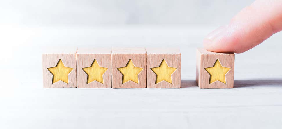 A close up shot of small wooden blocks lined side by side that have yellow stars engraved in them. One star has a figure over it and is off to the right, indicating a four-star review.
