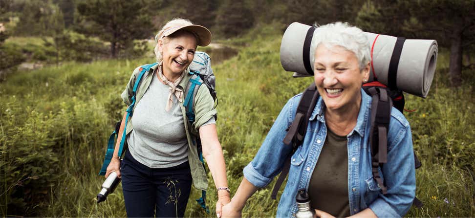 A lesbian senior female couple are outdoors hiking and holding hands.