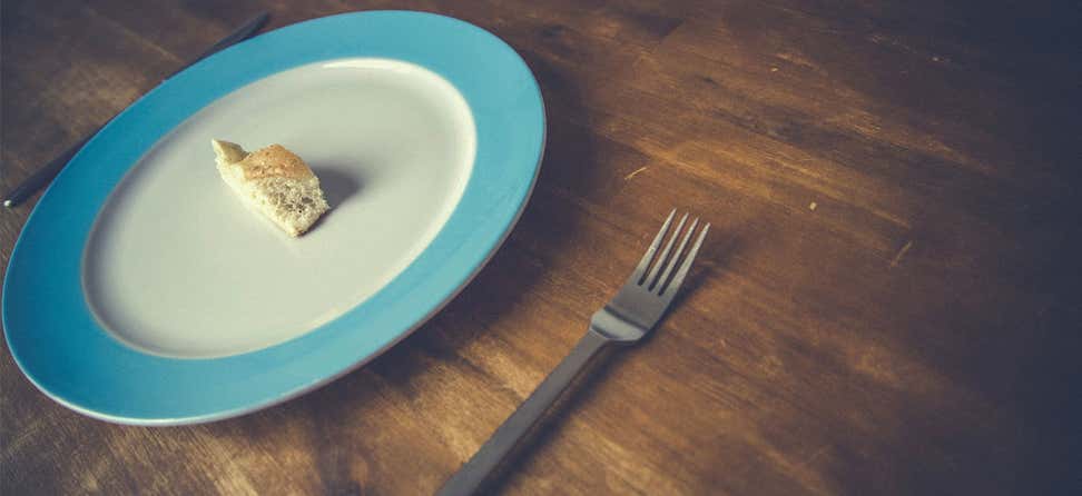 A lone piece of bread sits on an empty plate with a fork close by, indicating hunger.