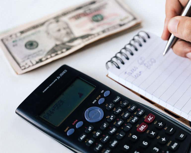 A close up shot of a calculator, pad of paper, and money - implying budgeting finances.