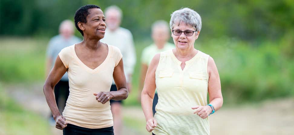 Two senior women are walking outside in the park, getting exercise together.