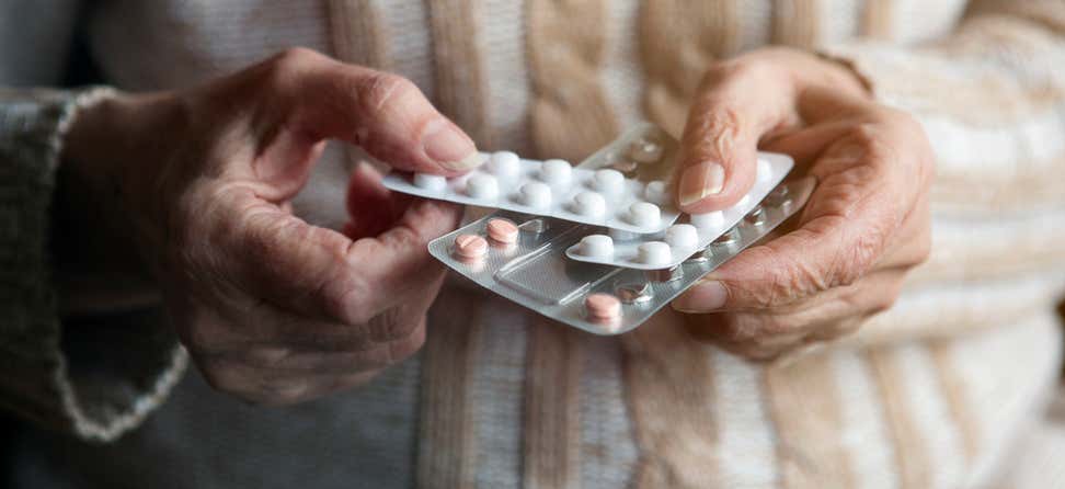 An up close shot of a senior man is holding a few packets of pills in his hands.