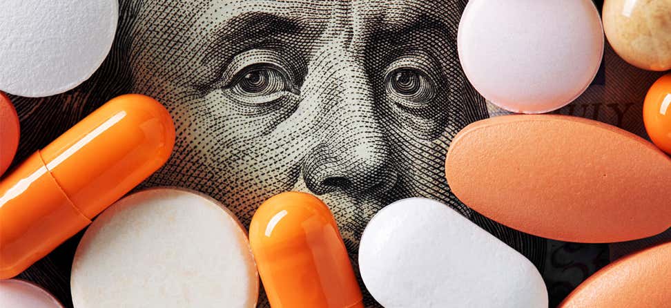 A hundred dollar bill, with Ben Franklin showing through, is surrounded with prescription pills.