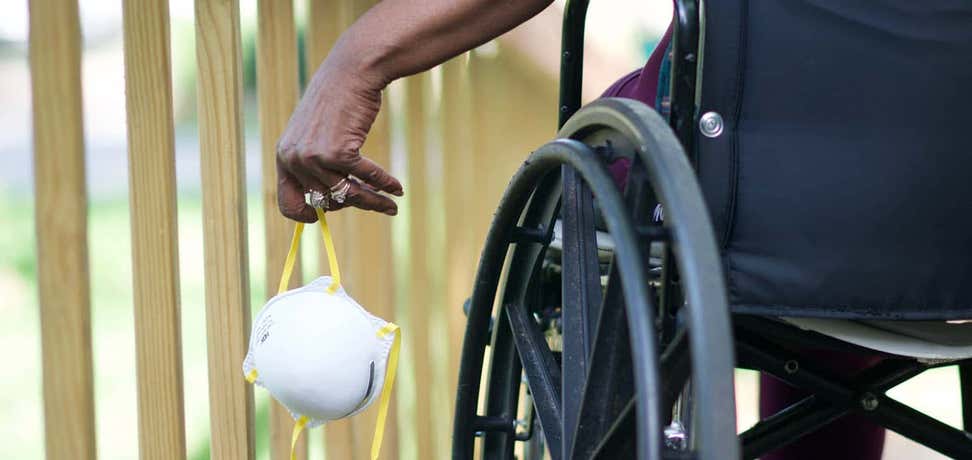 Close-up photo of an older black person in a wheelchair carrying an N95 mask.
