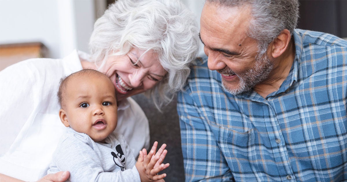 An interracial senior couple is playing with their grandson in their living room.