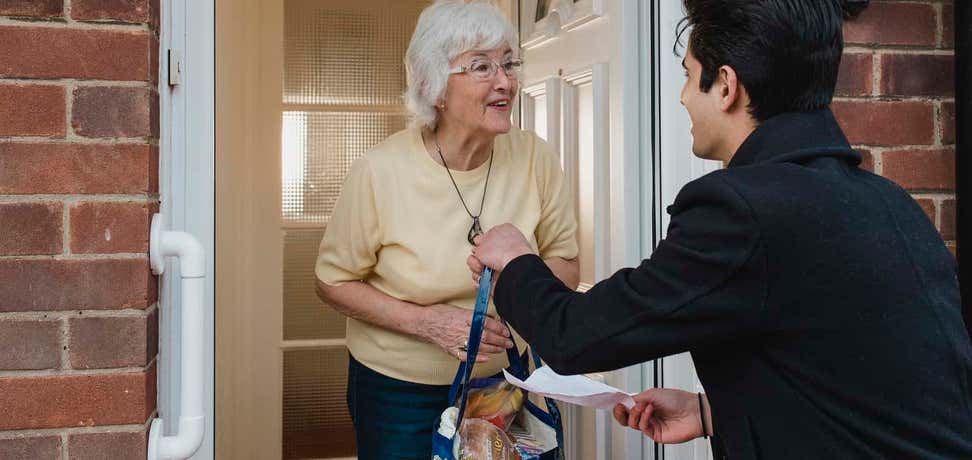Younger man delivering grocery bag of food to older woman's home