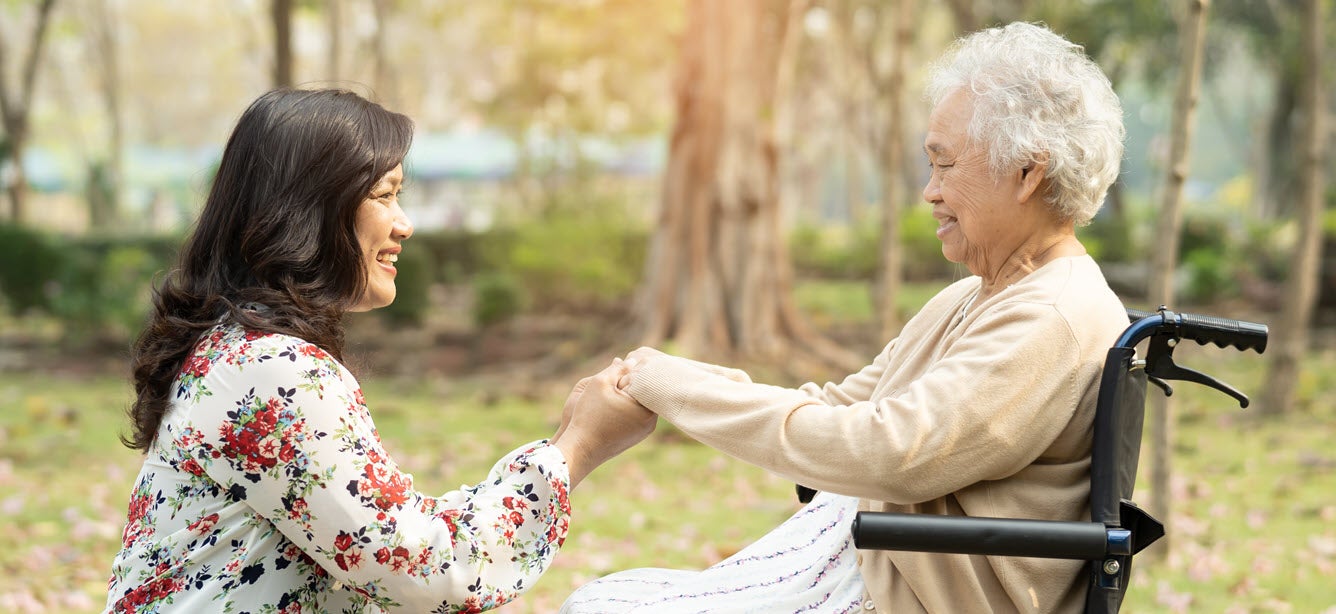 Asian daughter caregiver with senior in wheelchair outside