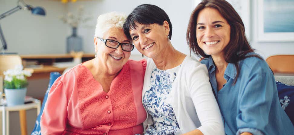A group of intergenerational women are sitting on the couch, smiling and posing for the camera.
