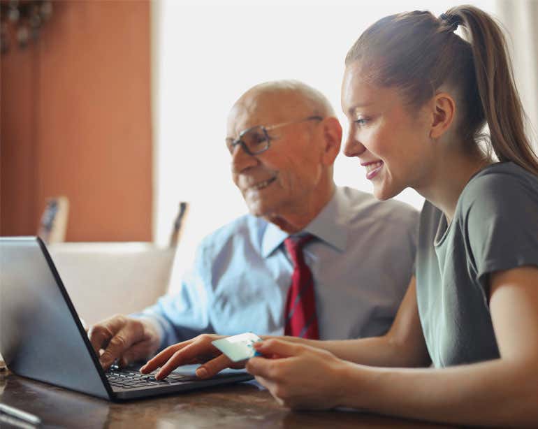 A younger benefits enrollment professional helps a senior find benefits options online.