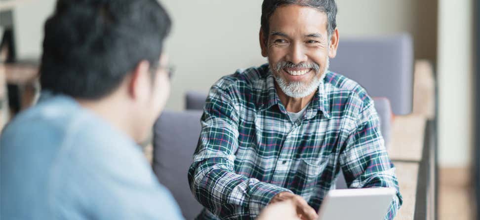 An older man wearing a plaid shirt is shaking hands with an advisor.