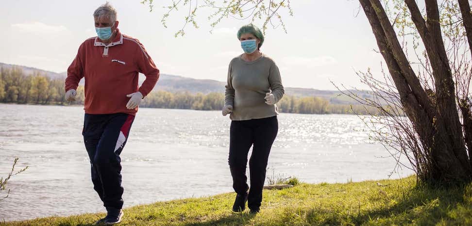 senior couple wearing masks during COVID pandemic goes for a jog by the river