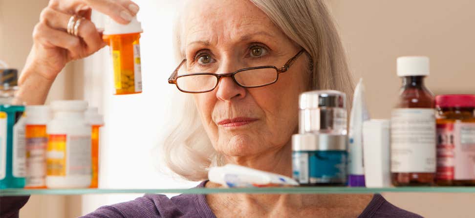 A senior woman is looking at prescription bottles in her bathroom.