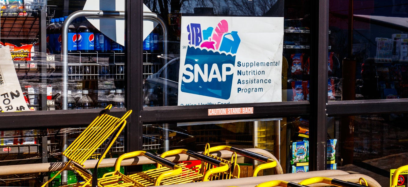 A "We Accept Supplemental Nutrition Assitance Program (SNAP)" sign appears on the window of a grocery retailer.