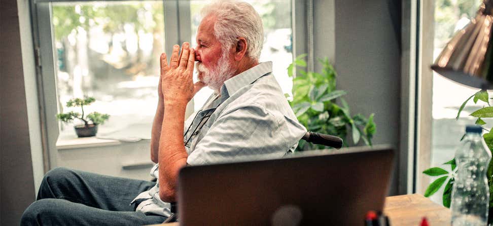 A senior caucasian man in a wheel chair is contemplating life's decisions in his home office.