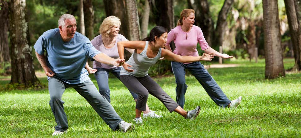 Three seniors and an instructor practice tai chi in a park.