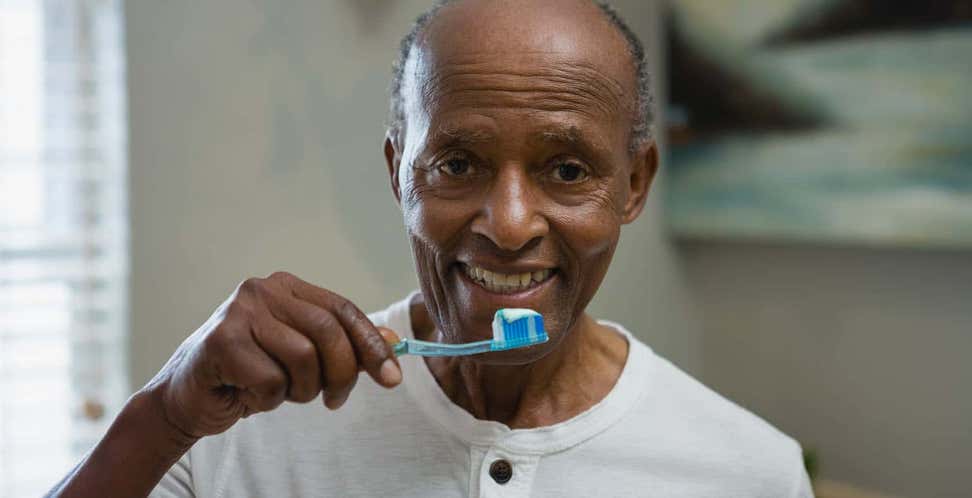 A senior Black man holds up a toothbrush as though he's ready to brush his teeth.