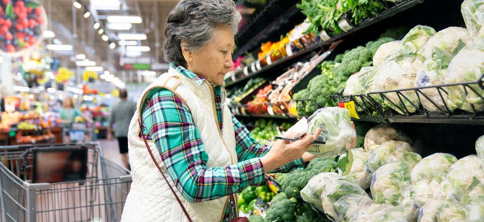 A senior Asian woman is looking at produce in the grocery store.