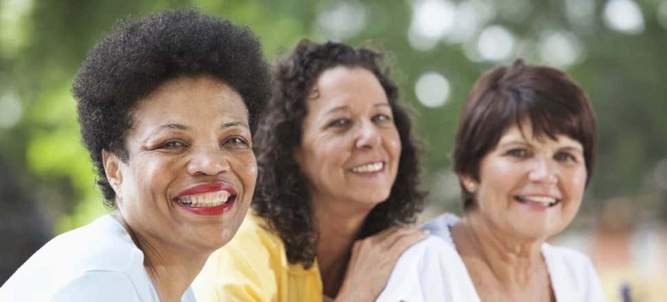 Three multi-ethnic women pose for the camera, all smiling. 
