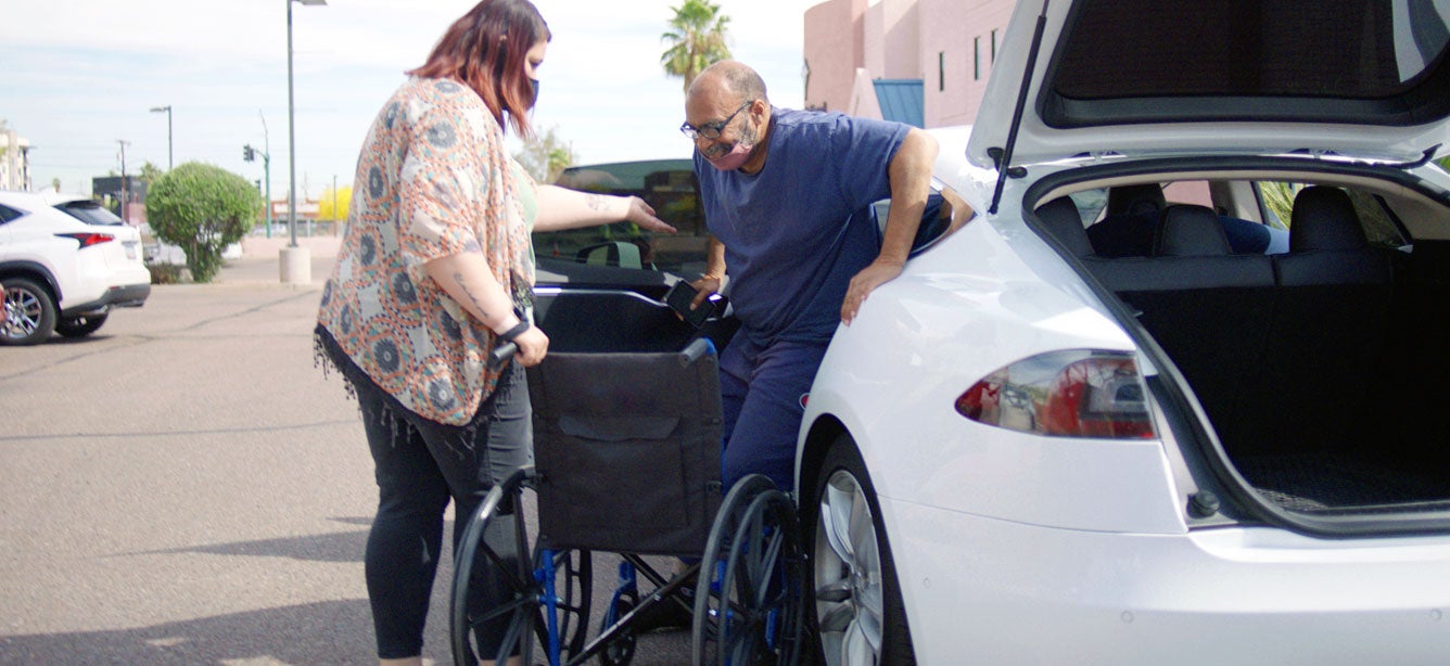 A Lyft driver helps a senior man get out of the car and into a wheel chair at a COVID-19 vaccine event in Arizona.
