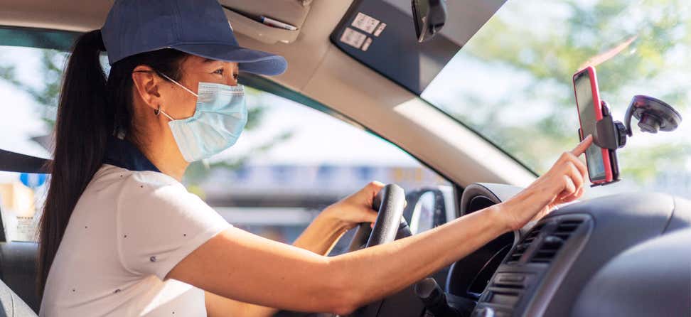 A female ridesharing driver checks her Lyft app for her next destination, while wearing a mask.